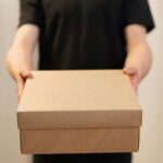 Close-up of a person holding a cardboard box, ideal for delivery service concepts.