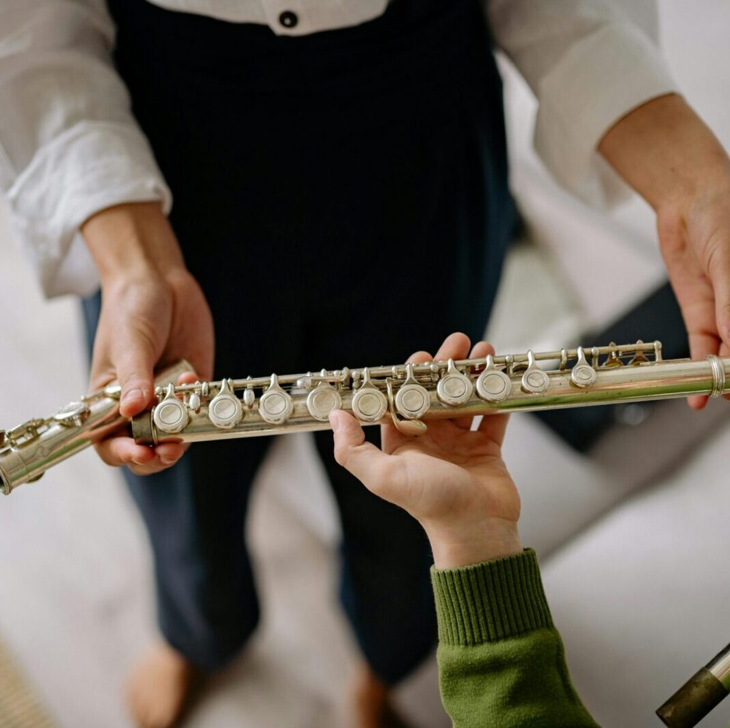 Teacher guiding child with flute playing, focusing on hands and instrument.