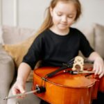 A young girl plays the cello at home, enjoying music indoors.