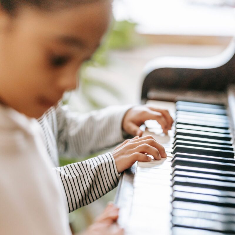 Side view of crop unrecognizable ethnic kids playing piano together in light room